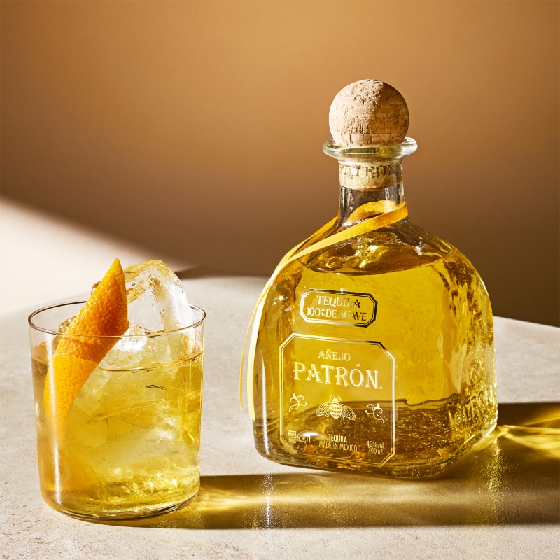 Patrón Añejo Tequila bottle and cocktail with an orange twist.